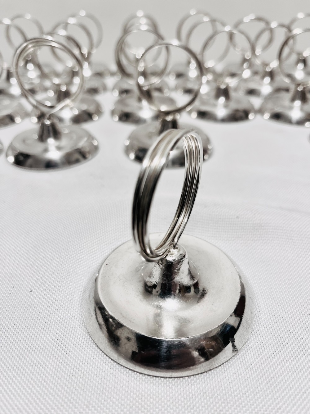 A collection of twenty-four silver-plated menu holders featuring domed bases and circular clip rings. View III