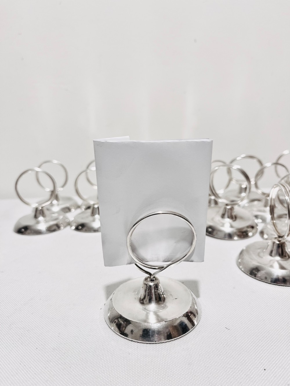 A collection of twenty-four silver-plated menu holders featuring domed bases and circular clip rings. View V
