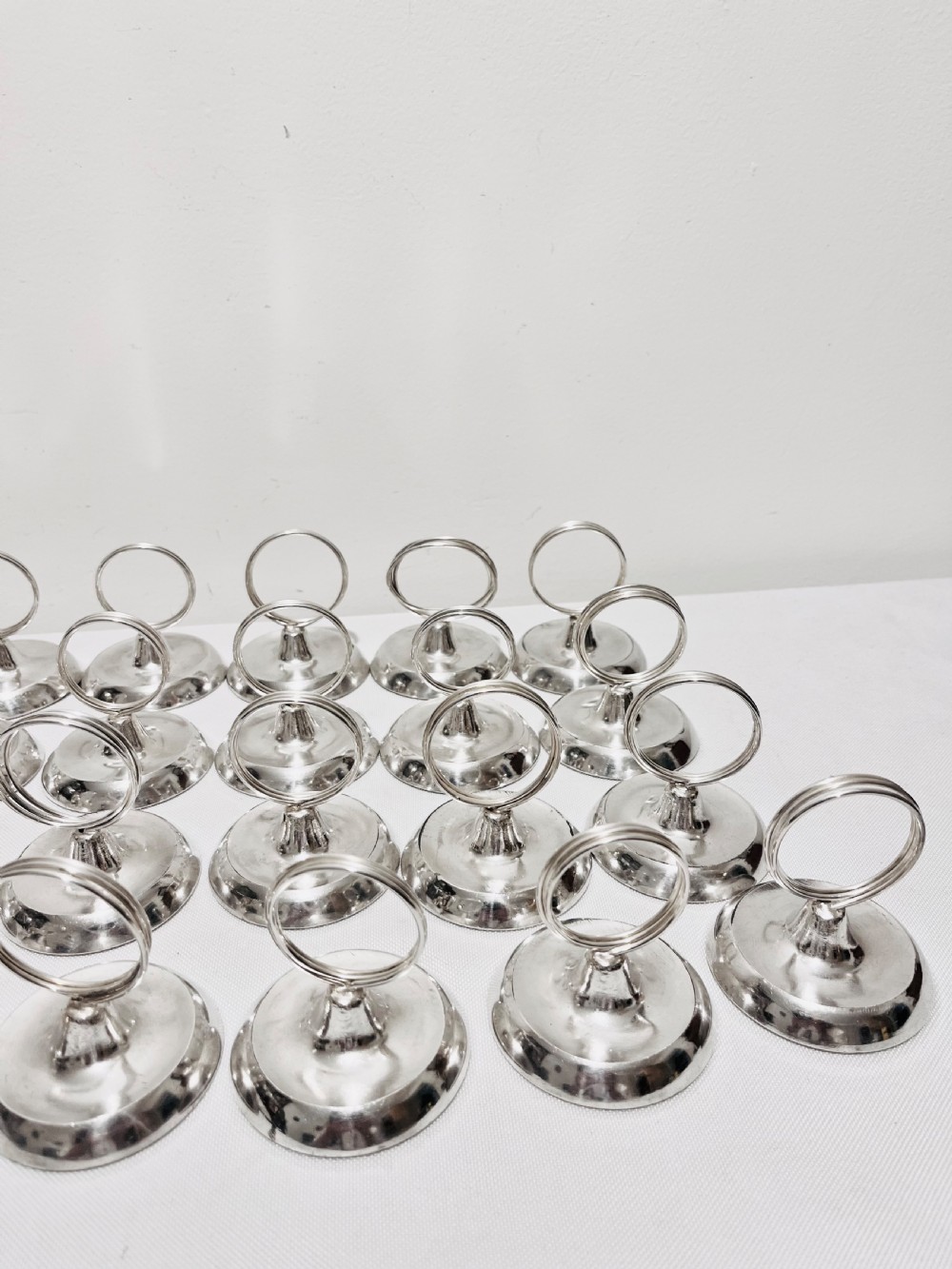 A collection of twenty-four silver-plated menu holders featuring domed bases and circular clip rings. View VII
