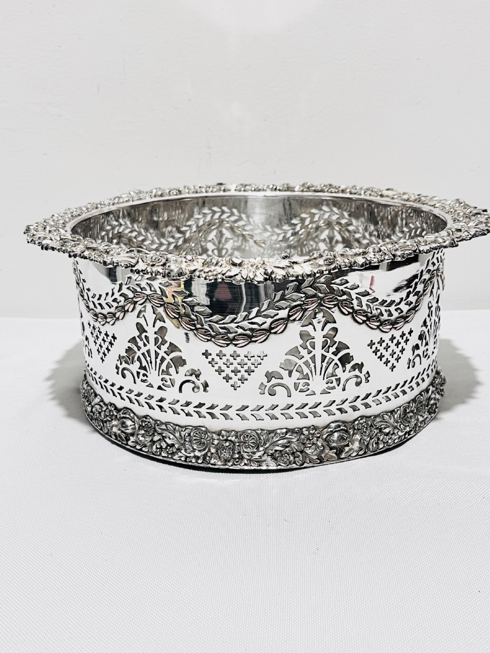 A large cylindrical antique silver-plated coaster featuring pierced reticulated fretwork, garland swags, and embossed floral borders.