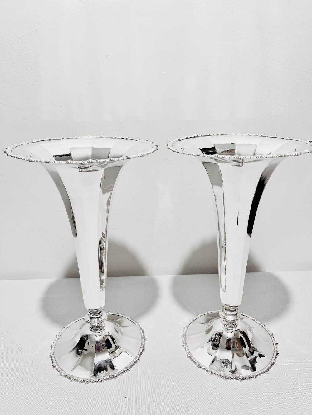 A pair of tall silver-plated trumpet vases featuring flared fluted rims, beaded border trims, and stepped circular bases.