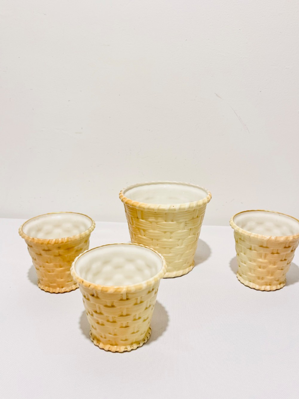 An Edwardian silver-plated tiered stand holding four cream basketweave ceramic pots on scrolling wirework supports. View III