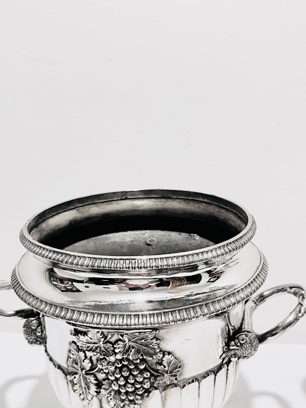 A pair of Regency silver-plated urn-shaped wine coolers featuring raised grapevine motifs, gadrooned rims, fluted bases, and twin side handles. View VI