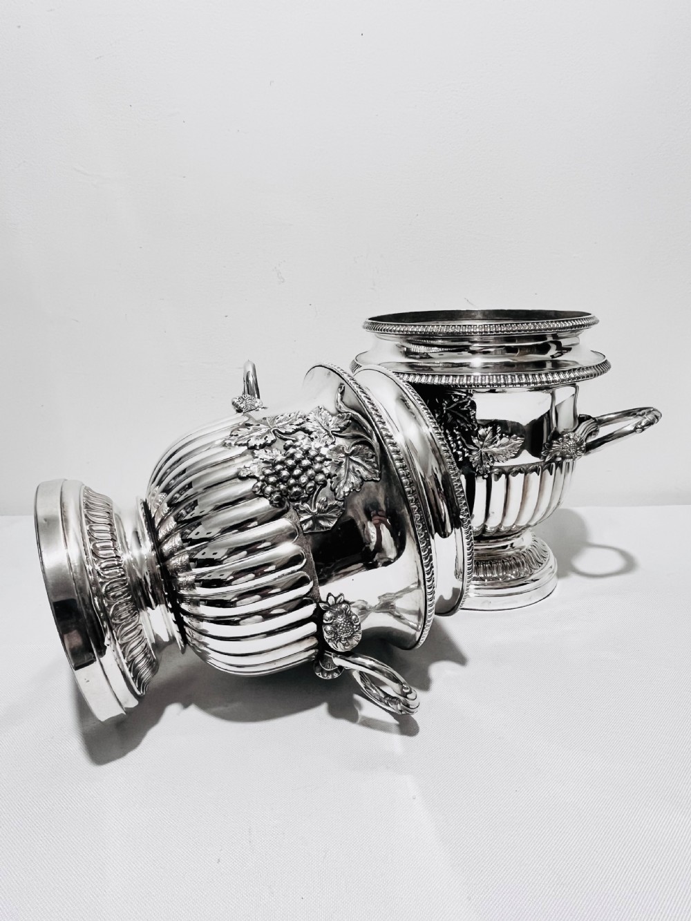 A pair of Regency silver-plated urn-shaped wine coolers featuring raised grapevine motifs, gadrooned rims, fluted bases, and twin side handles. View VII