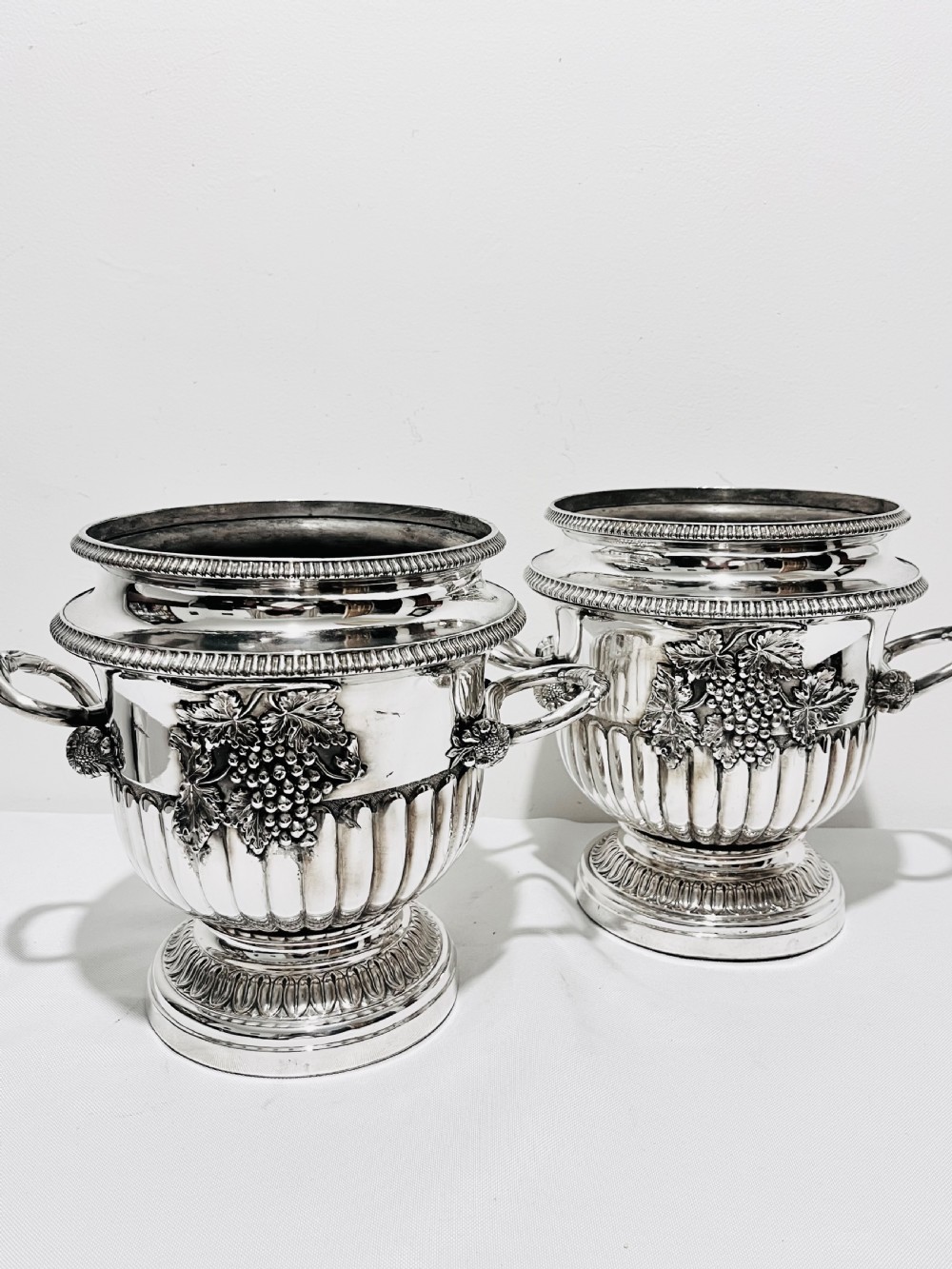 A pair of Regency silver-plated urn-shaped wine coolers featuring raised grapevine motifs, gadrooned rims, fluted bases, and twin side handles. View VIII