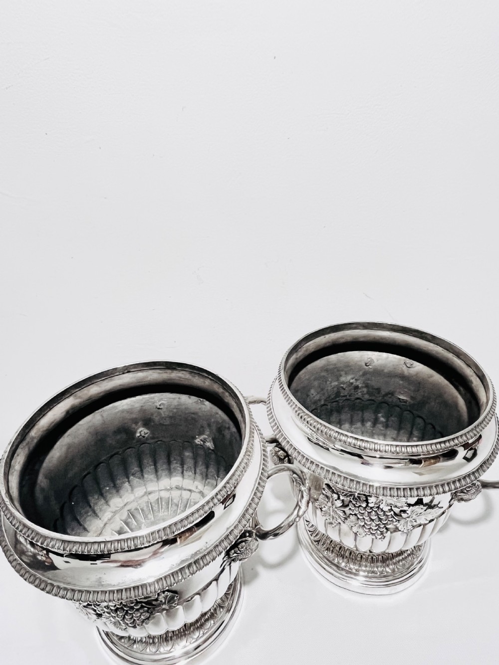 A pair of Regency silver-plated urn-shaped wine coolers featuring raised grapevine motifs, gadrooned rims, fluted bases, and twin side handles. View IX