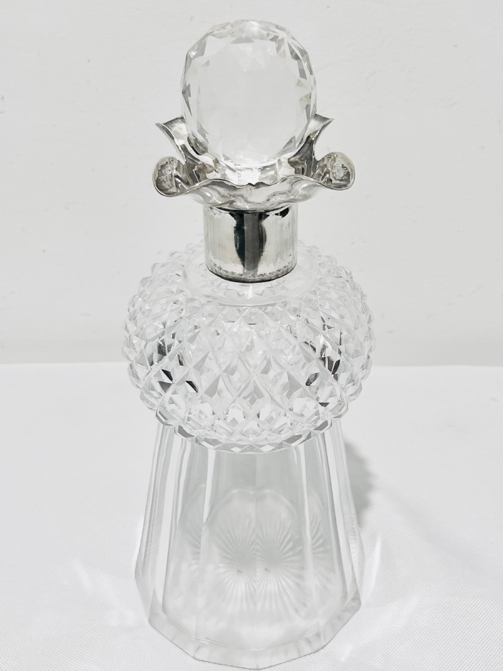 A clear cut glass spirit decanter shaped like a Scottish thistle with a fluted silver-plated metal collar and a faceted spherical glass stopper.