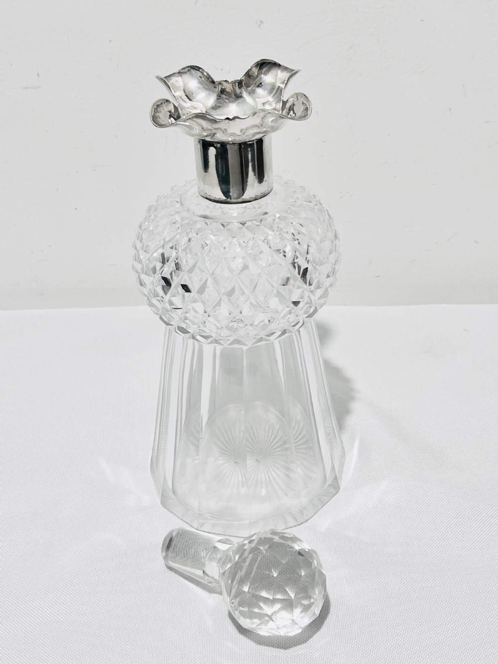 A clear cut glass spirit decanter shaped like a Scottish thistle with a fluted silver-plated metal collar and a faceted spherical glass stopper. View V