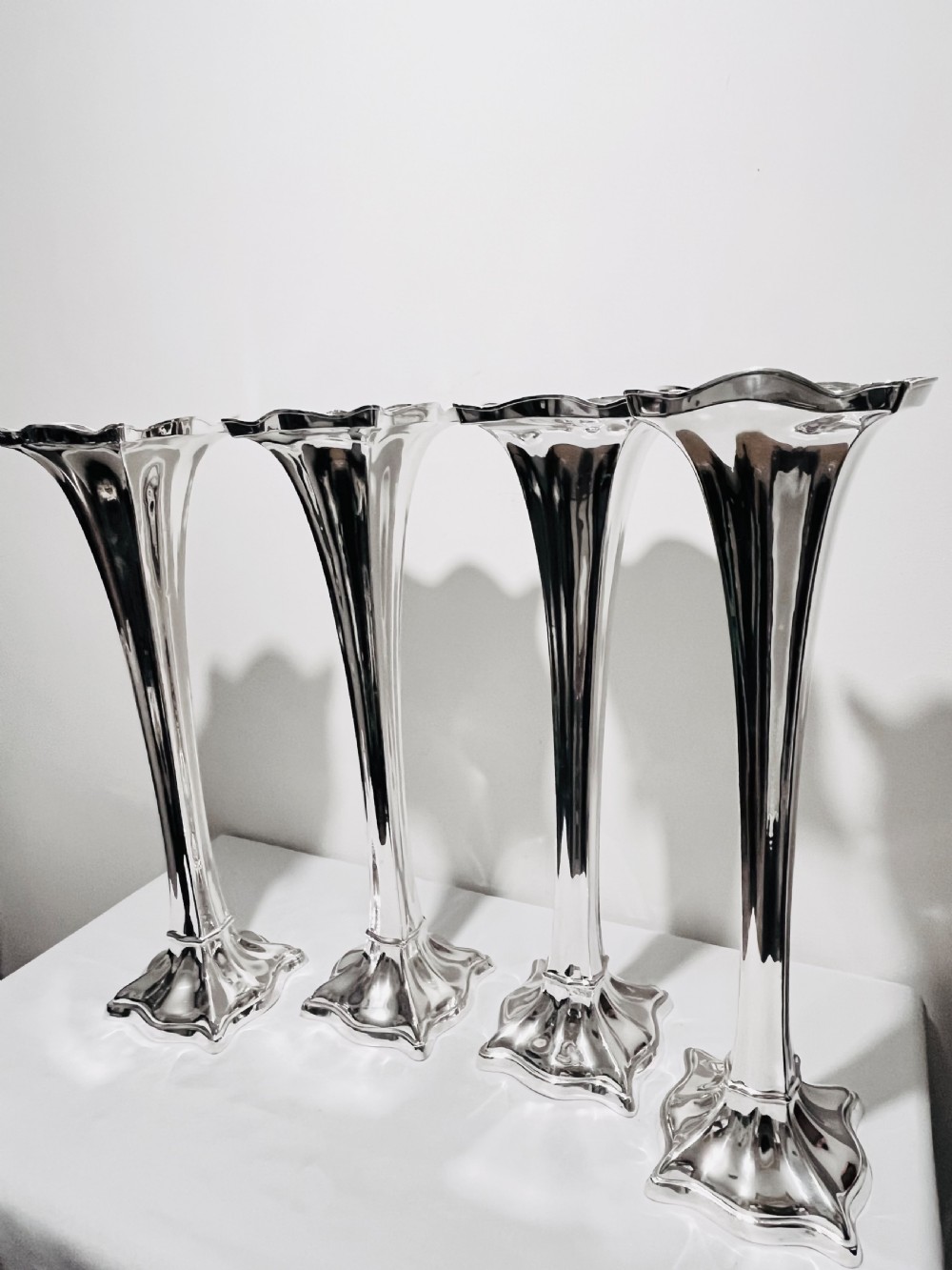 A set of four tall polished silver-plated trumpet vases featuring fluted stems, scalloped rims, and flared stepped bases. View III