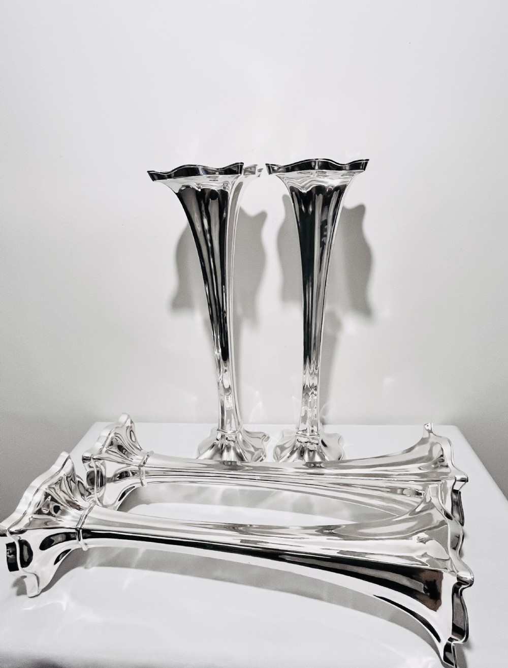 A set of four tall polished silver-plated trumpet vases featuring fluted stems, scalloped rims, and flared stepped bases. View V