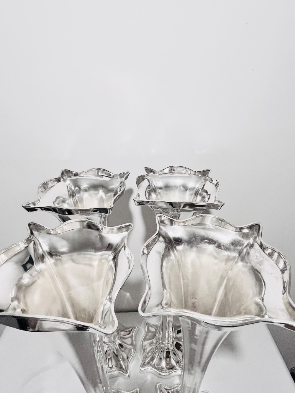 A set of four tall polished silver-plated trumpet vases featuring fluted stems, scalloped rims, and flared stepped bases. View VI