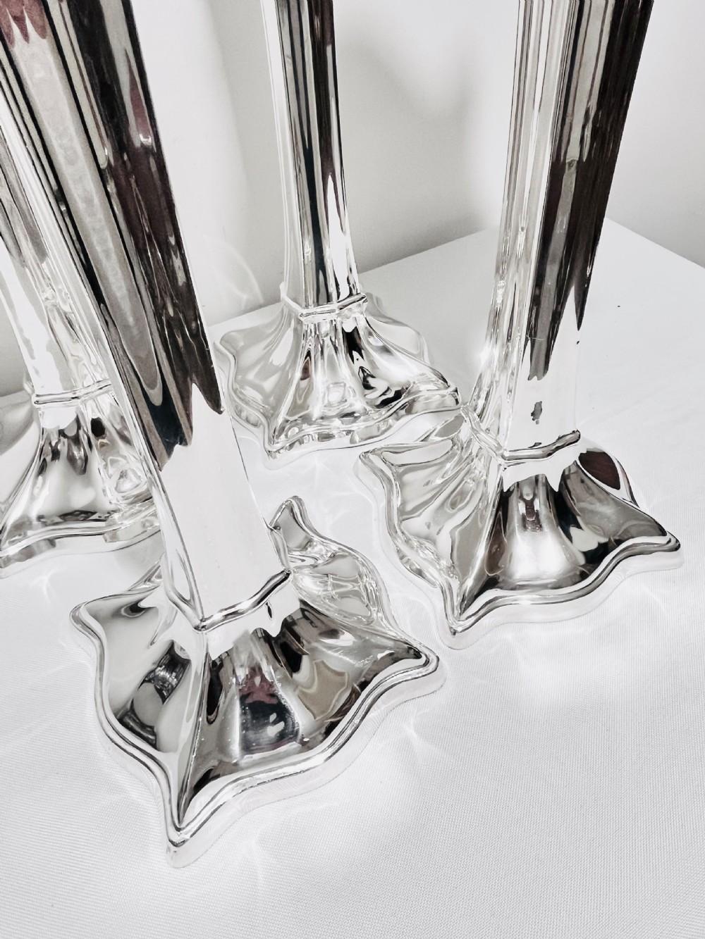 A set of four tall polished silver-plated trumpet vases featuring fluted stems, scalloped rims, and flared stepped bases. View VII