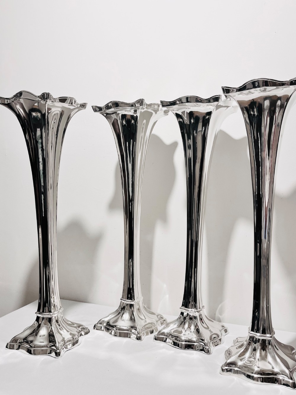 A set of four tall polished silver-plated trumpet vases featuring fluted stems, scalloped rims, and flared stepped bases. View VIII