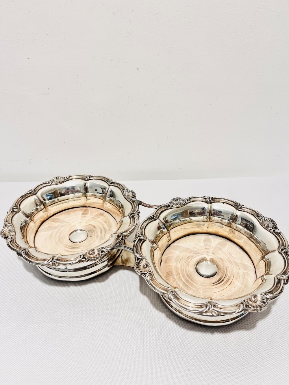 An antique Old Sheffield silver plate double wine decanter trolley with shell and scroll borders and turned wooden inserts.