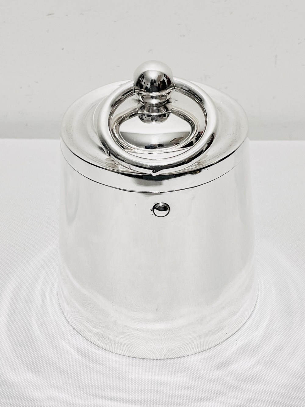 A polished silver plated cylindrical biscuit box designed in the form of a trade weight, featuring a fitted lid with a central ring handle.