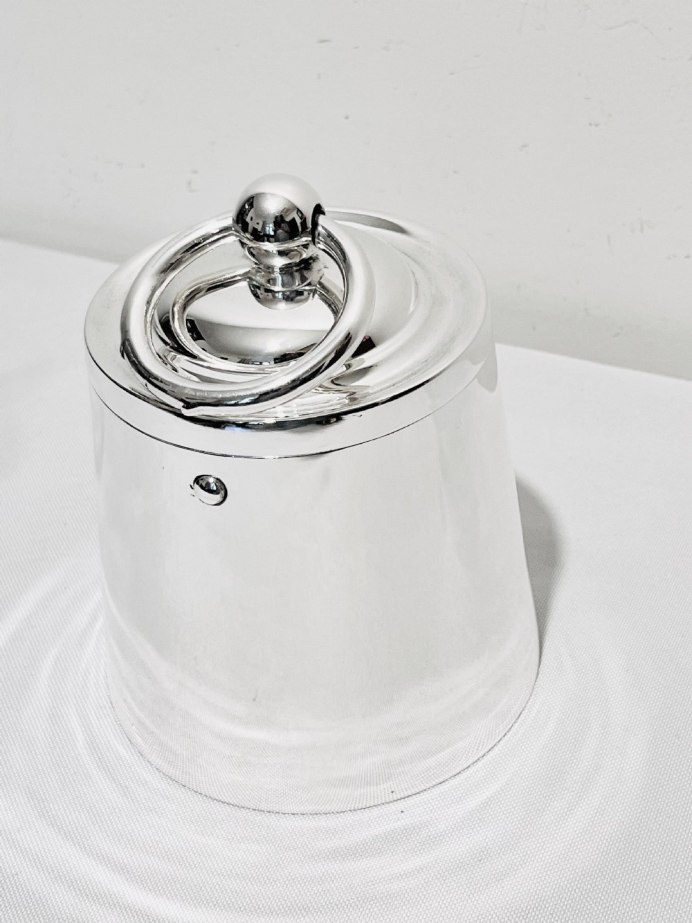 A polished silver plated cylindrical biscuit box designed in the form of a trade weight, featuring a fitted lid with a central ring handle. View III