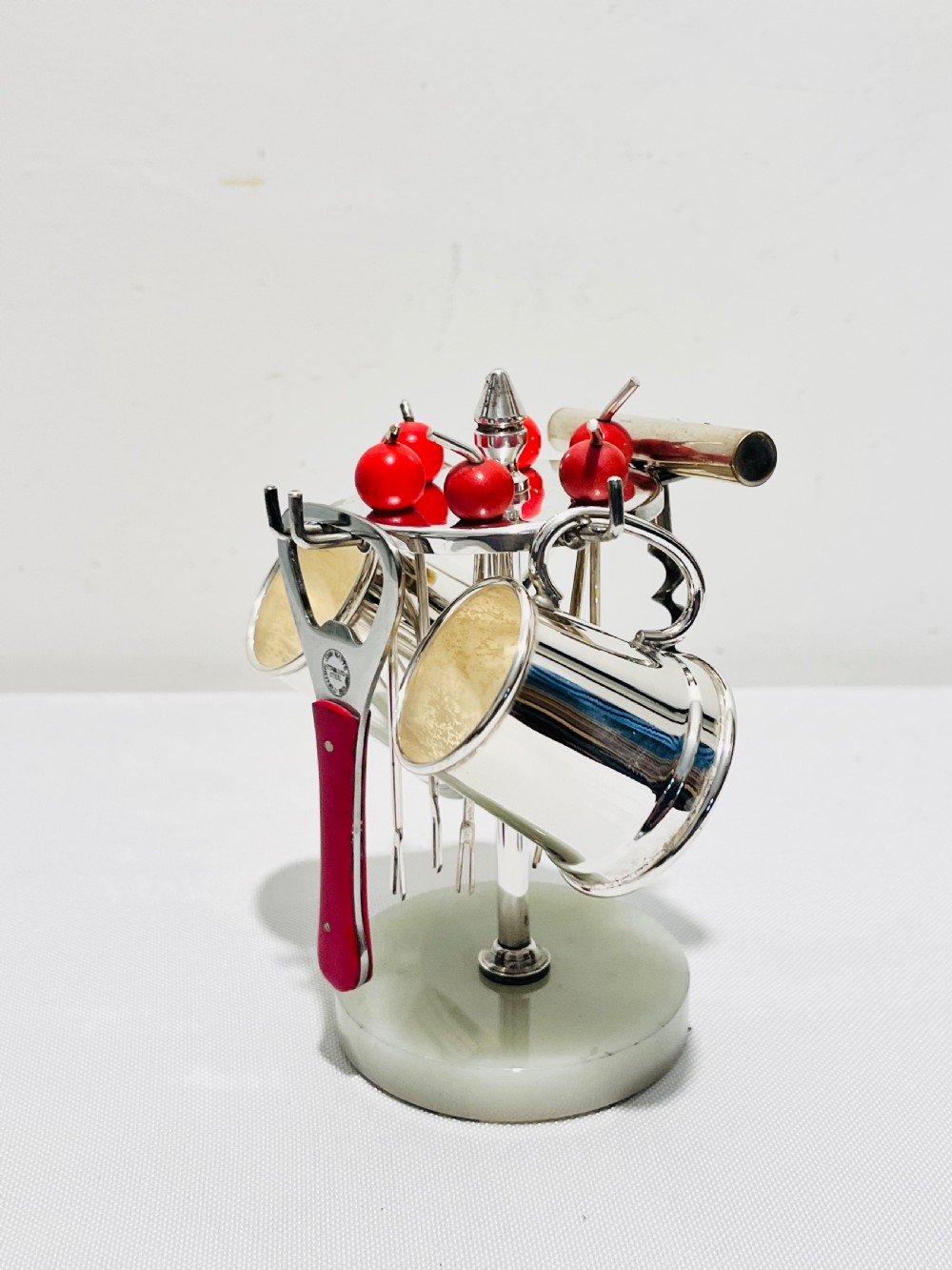 An Art Deco silver-plated bar set featuring miniature tankards, red-handled tools, and cherry cocktail picks arranged on a circular stand with a pale onyx base.
