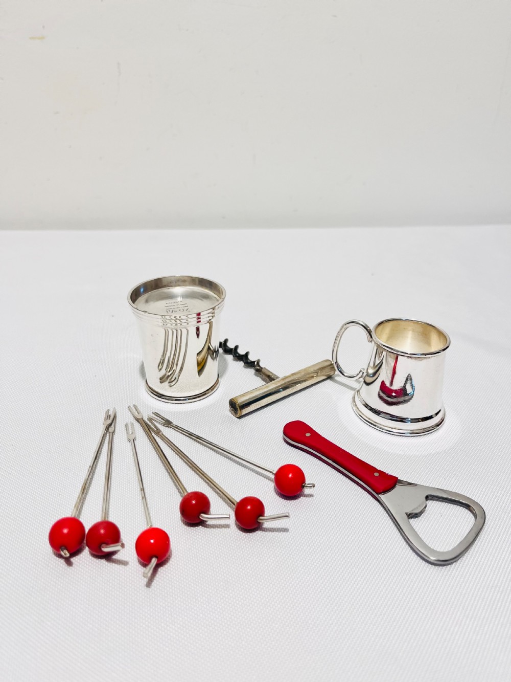 An Art Deco silver-plated bar set featuring miniature tankards, red-handled tools, and cherry cocktail picks arranged on a circular stand with a pale onyx base. View III