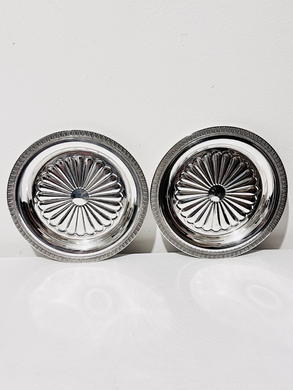 A pair of circular French silver-plated wine coasters featuring fluted central wells and detailed outer rims.