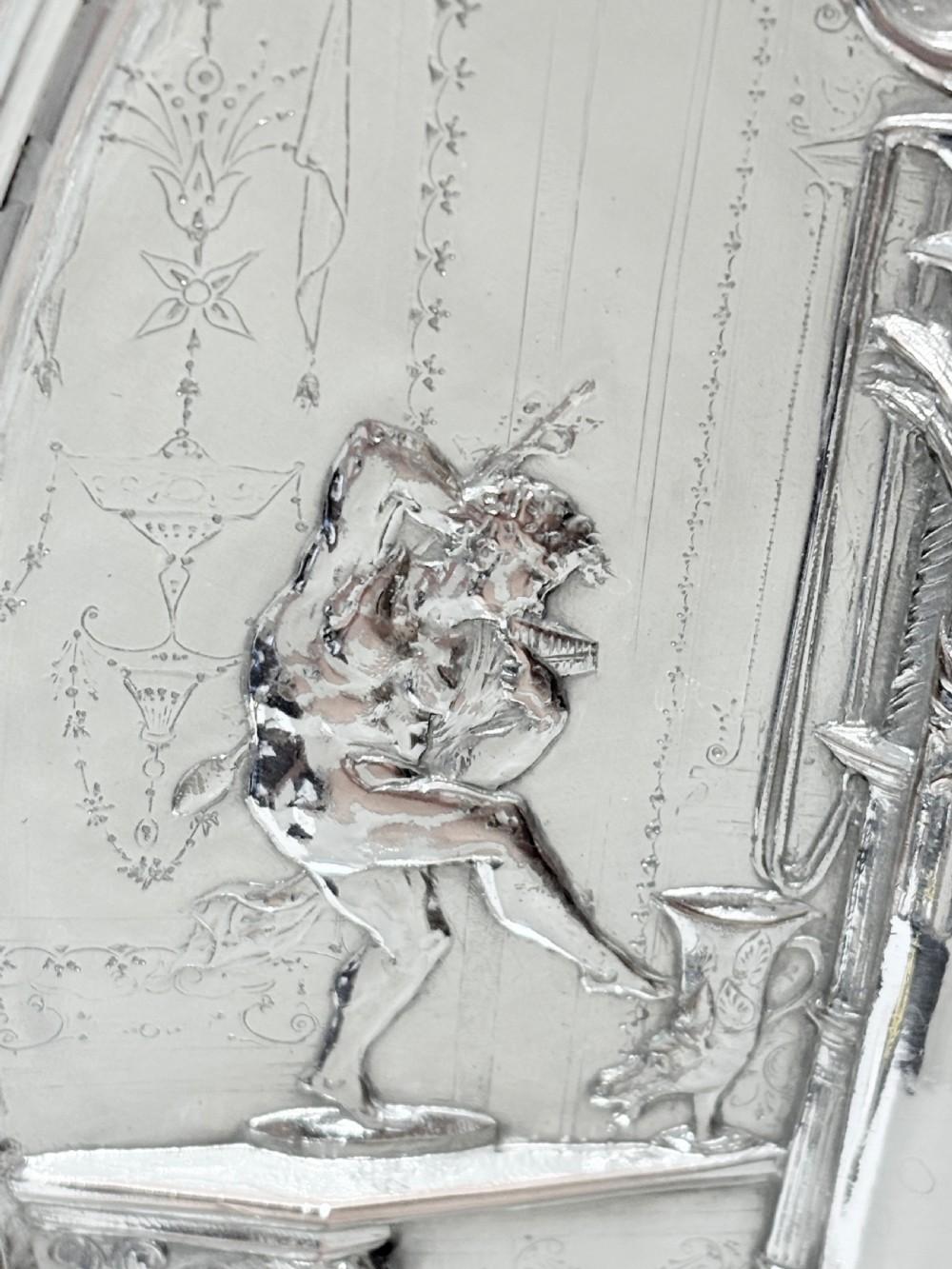 A circular silver plate electrotype charger featuring a detailed relief depiction of classical figures framed by ornate scrolled borders. View IX