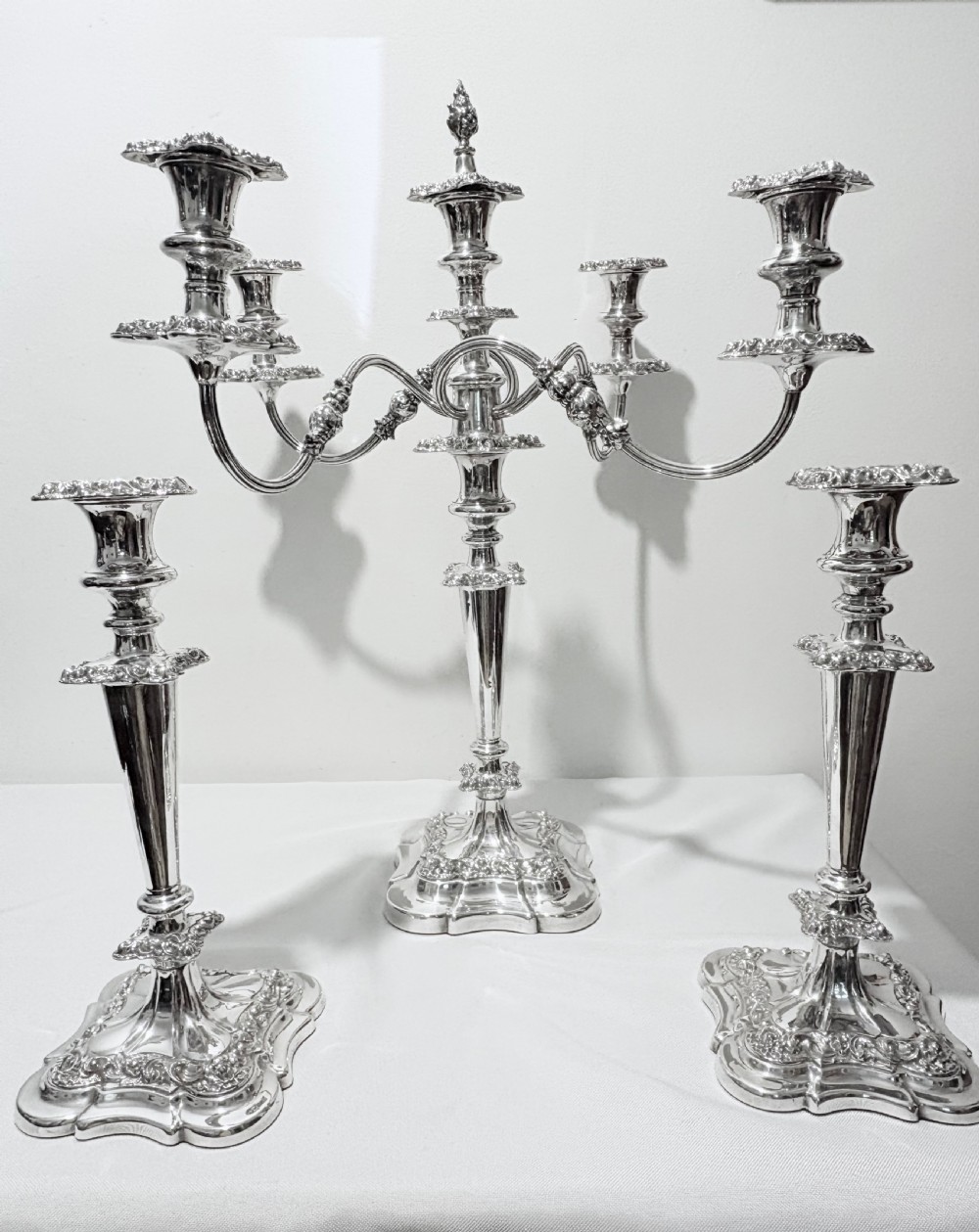A three-piece antique silver-plated candelabra suite consisting of a central five-light branch candelabrum flanked by two matching single candlesticks.