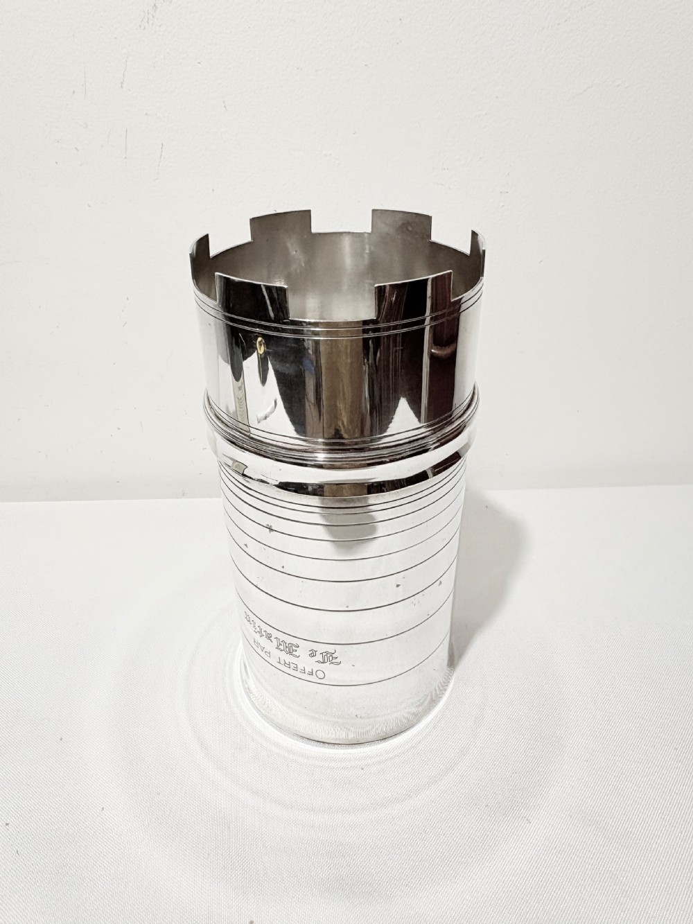 A cylindrical silver-plated wine holder featuring horizontal ring mouldings, an engraved French inscription, and a crenellated top rim.