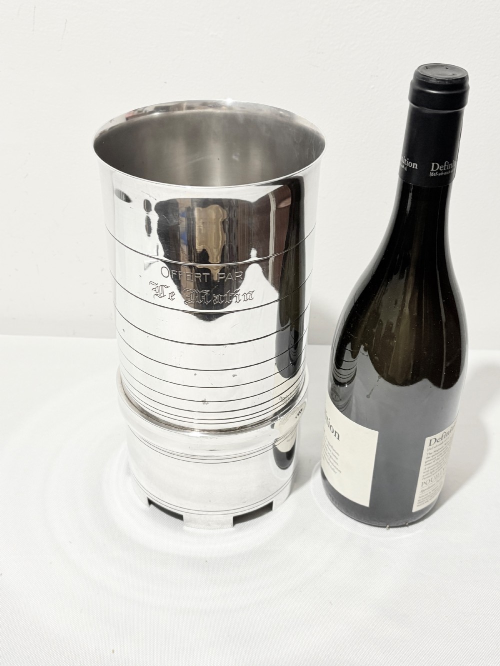 A cylindrical silver-plated wine holder featuring horizontal ring mouldings, an engraved French inscription, and a crenellated top rim. View II