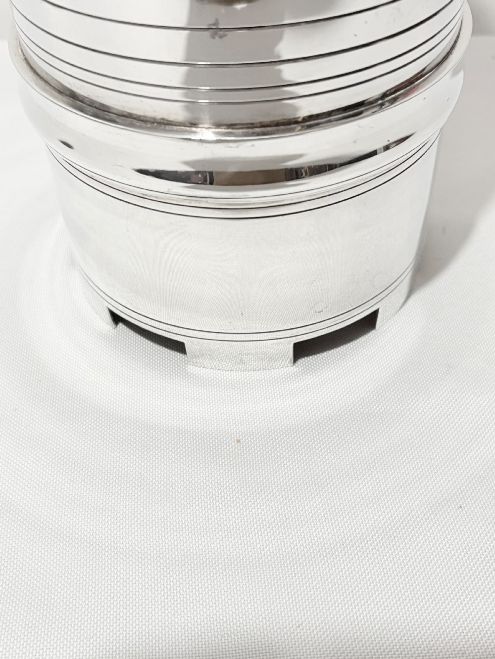 A cylindrical silver-plated wine holder featuring horizontal ring mouldings, an engraved French inscription, and a crenellated top rim. View III