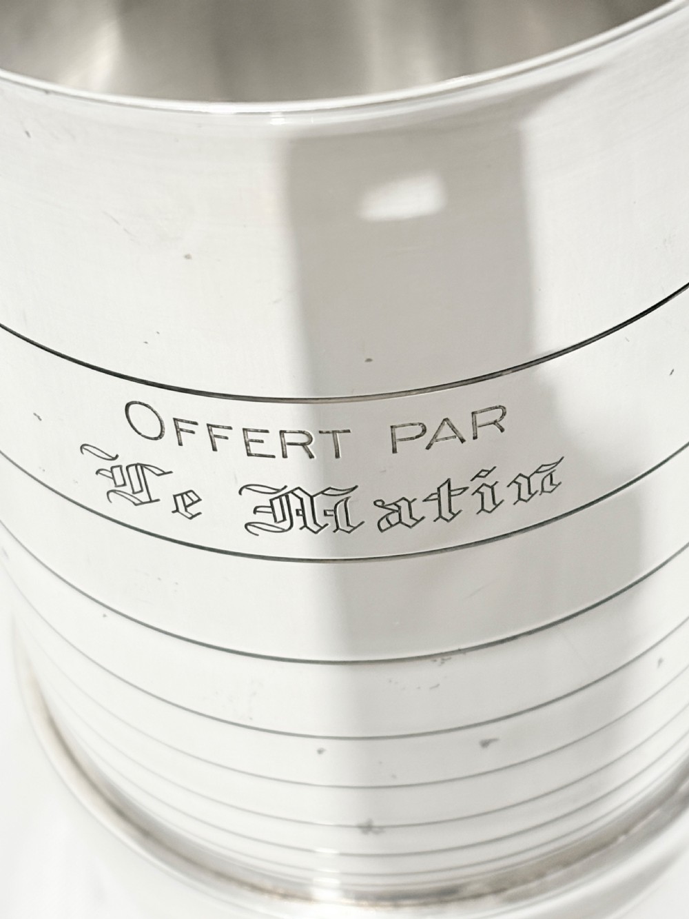 A cylindrical silver-plated wine holder featuring horizontal ring mouldings, an engraved French inscription, and a crenellated top rim. View VI