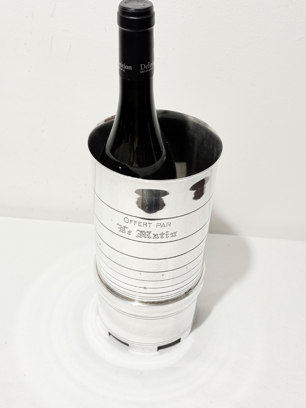 A cylindrical silver-plated wine holder featuring horizontal ring mouldings, an engraved French inscription, and a crenellated top rim. View VII