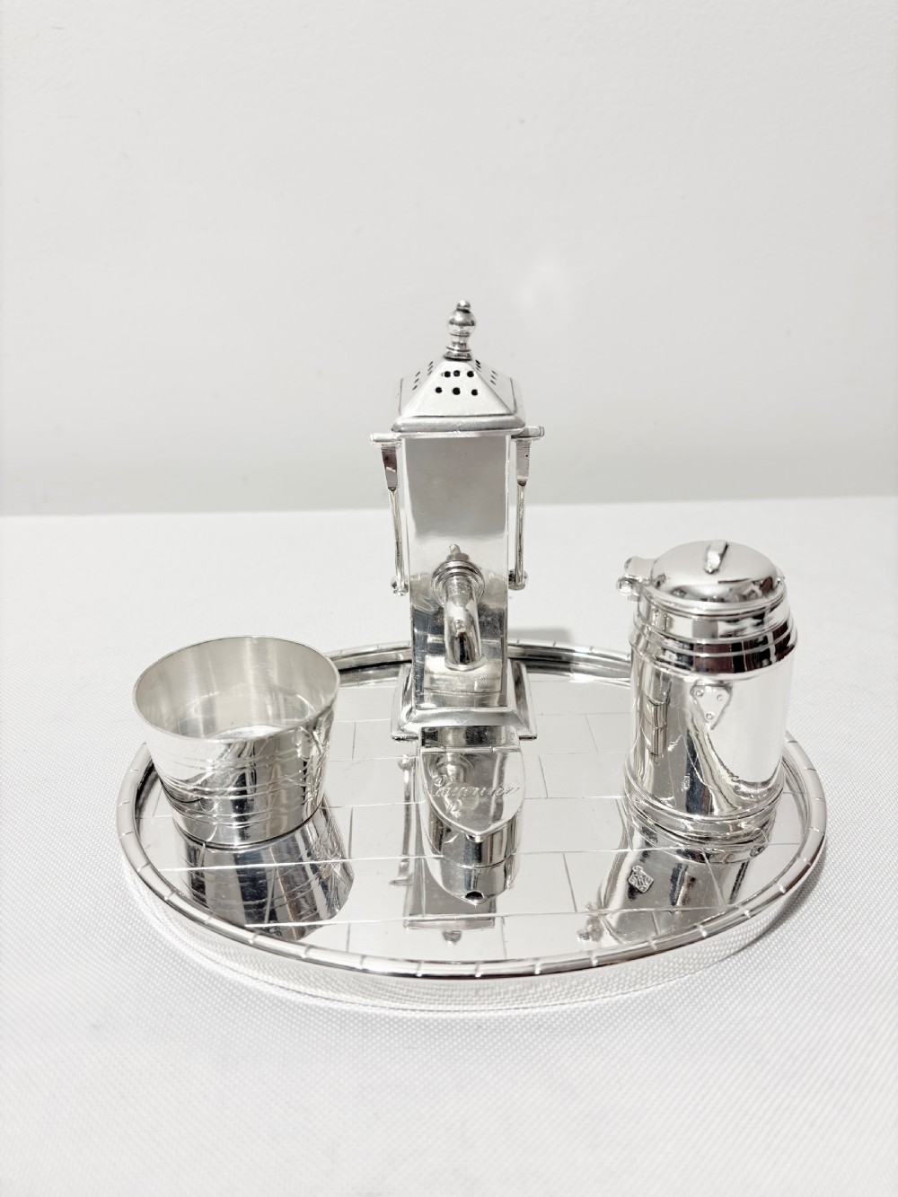 A Victorian silver-plated novelty cruet set featuring a central water pump pepper caster, a bucket salt cellar, and a milk churn mustard pot on a circular engraved tray.