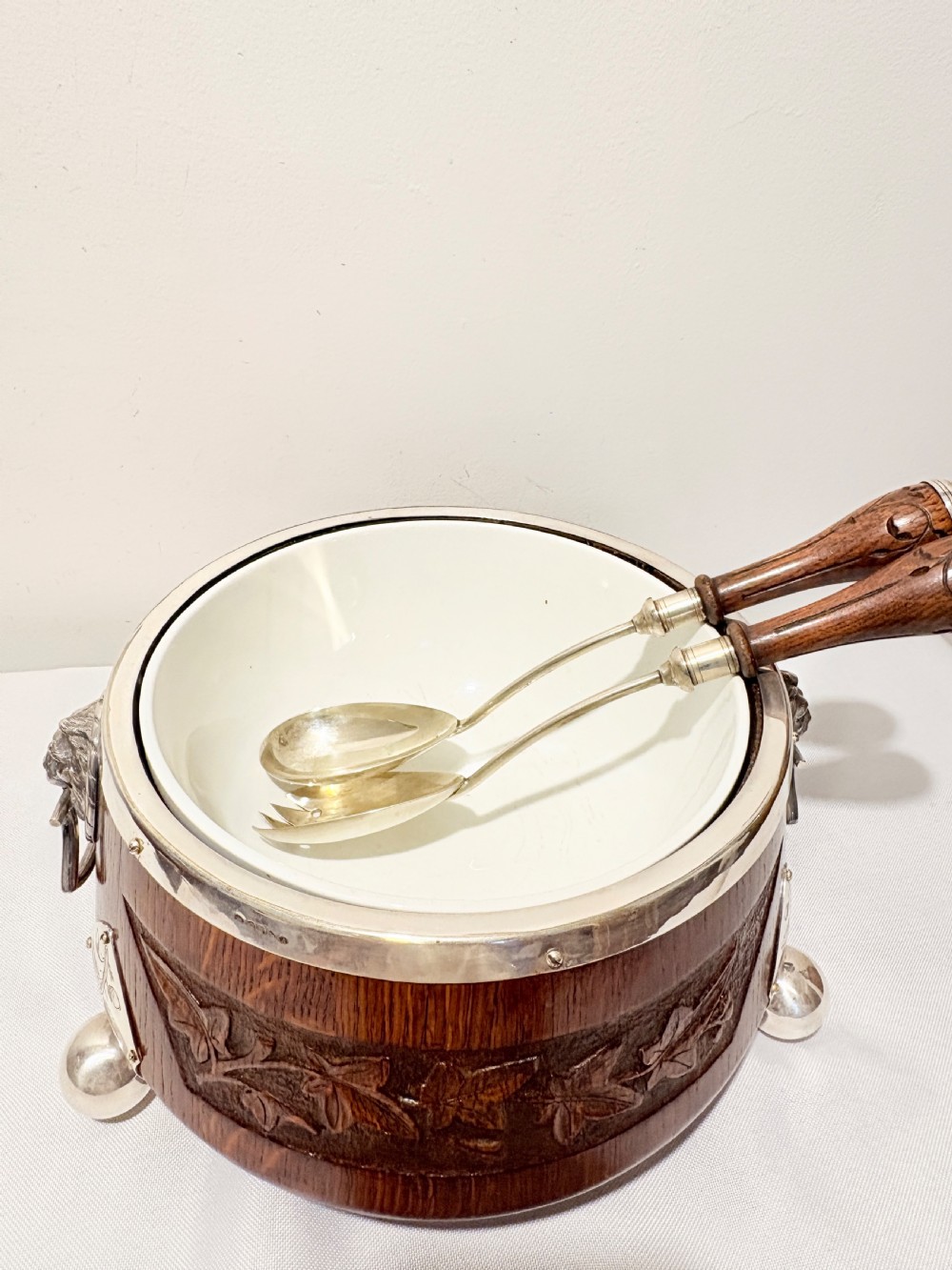 A late Victorian carved oak salad bowl with silver-plated rim, ball feet, and a white ceramic liner, featuring an ivy leaf carved band around the exterior. View V