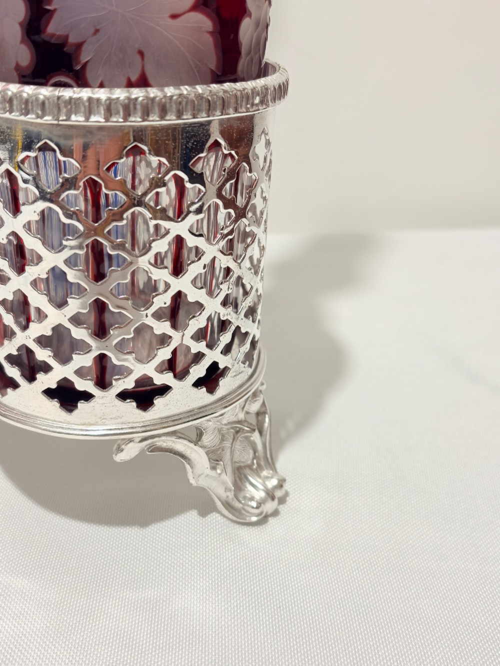 A Victorian silver-plated decanter stand holding three colourful cut-to-clear glass bottles in pink, blue, and deep red with faceted stoppers. View II