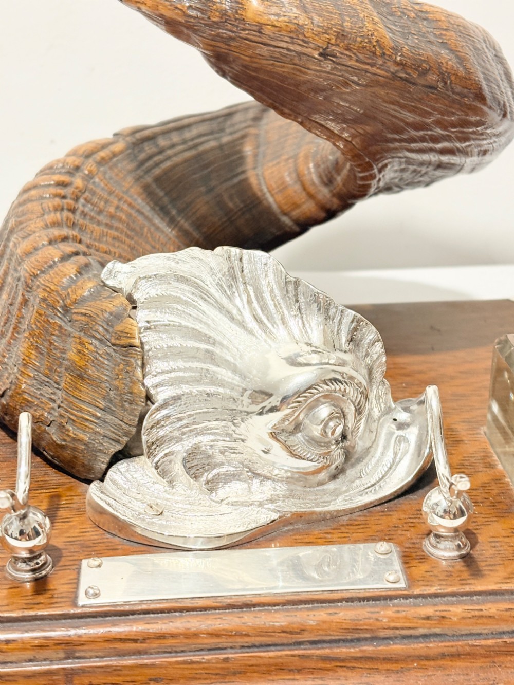 A Victorian era desk inkstand featuring a centrally mounted curled ram horn on an oak base with silver plated corner mounts and two glass inkwells. View II