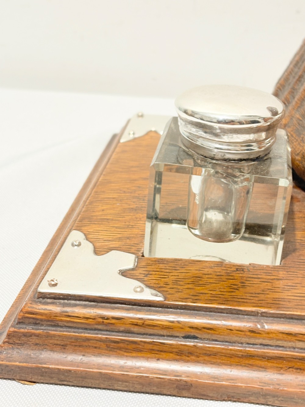 A Victorian era desk inkstand featuring a centrally mounted curled ram horn on an oak base with silver plated corner mounts and two glass inkwells. View VI