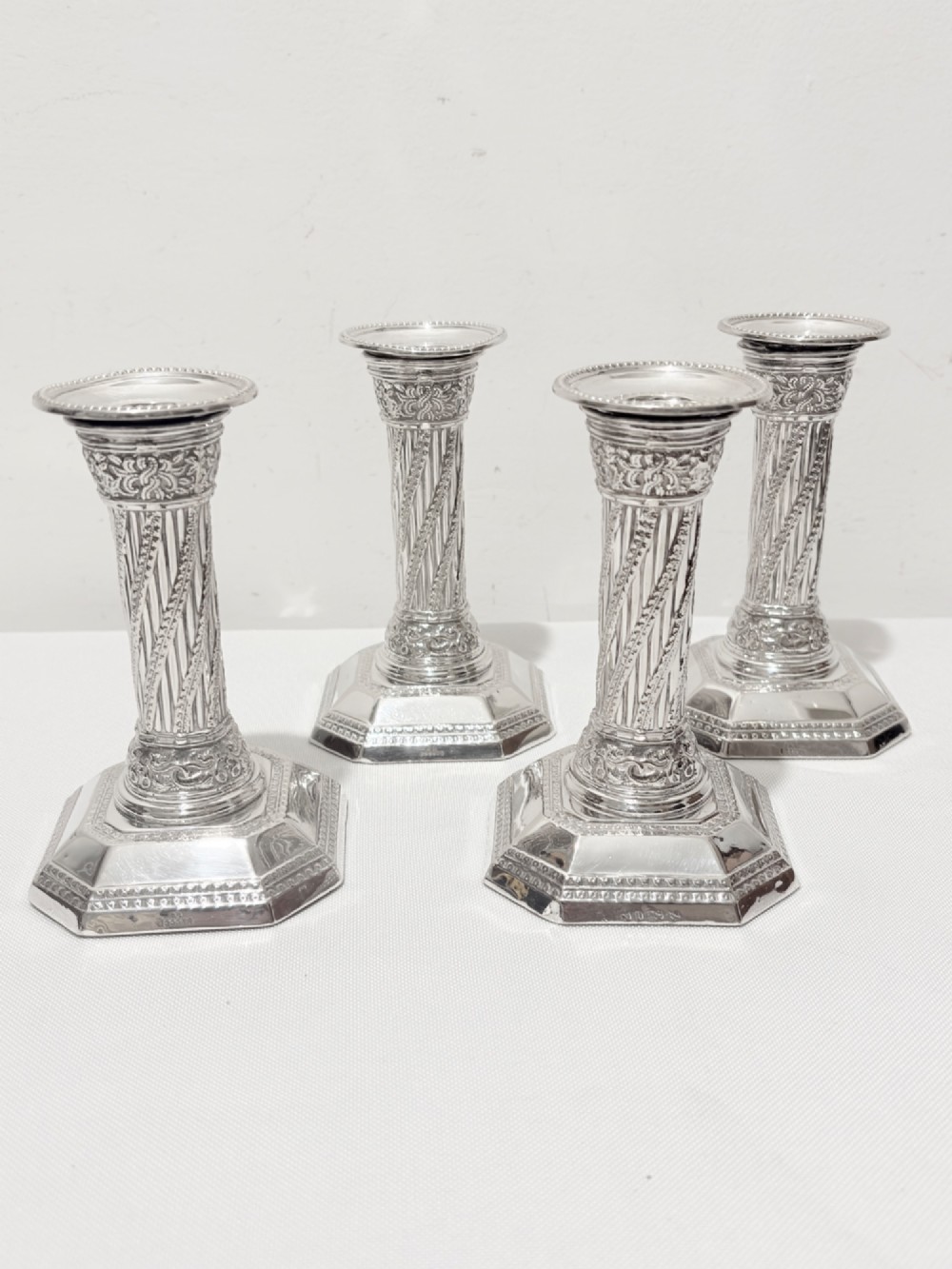 A set of four matching silver column candlesticks with spiral fluted stems and decorated octagonal bases.