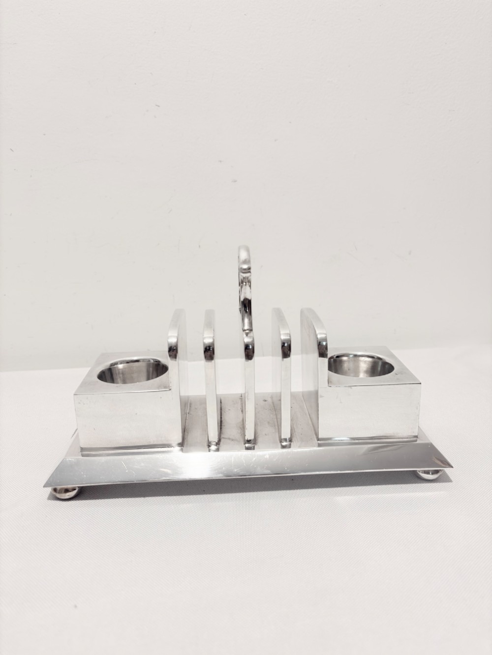 A Victorian silver-plated toast rack with radiator-style dividers flanked by two integrated egg holders on a rectangular base with ball feet.