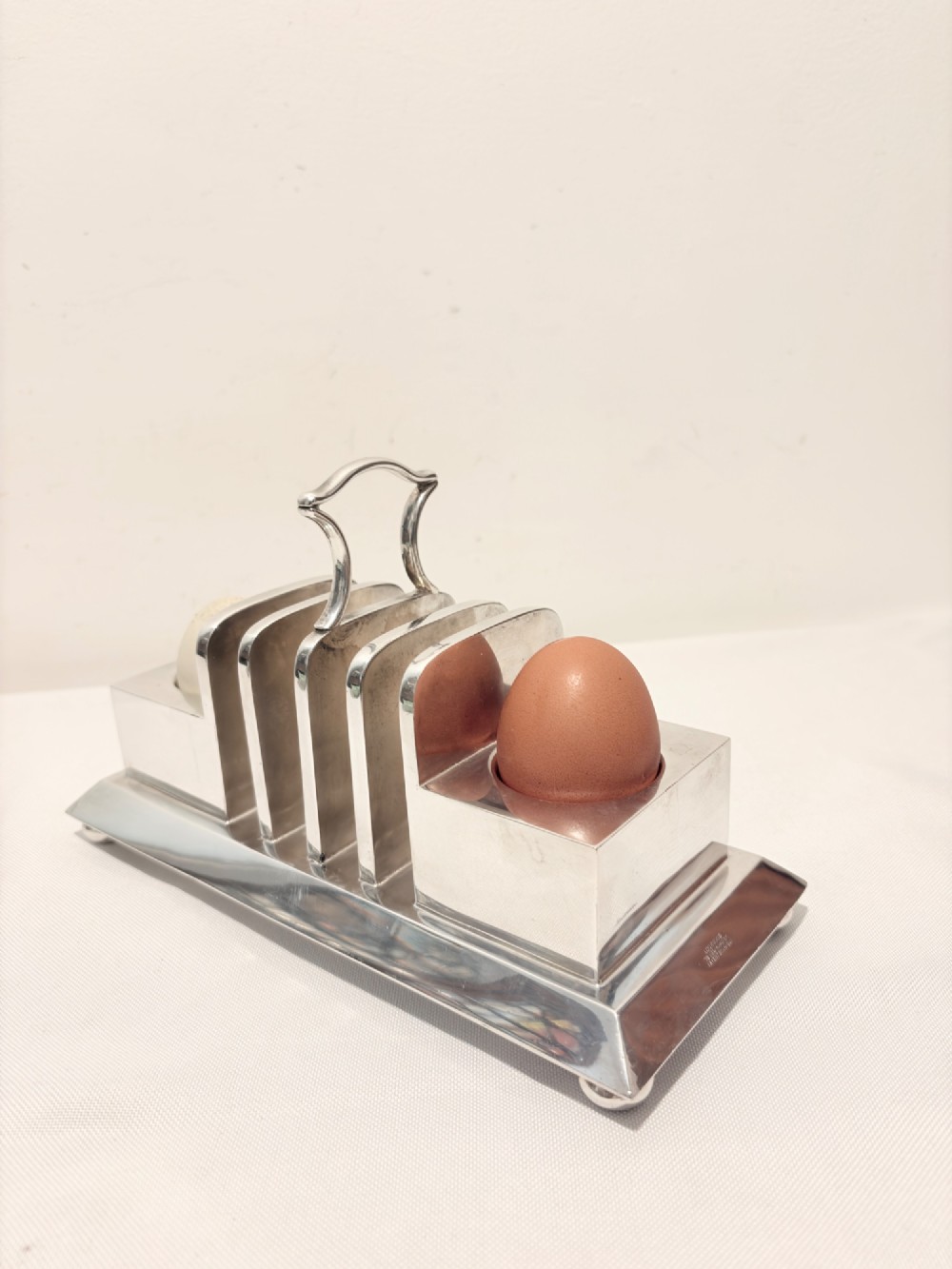 A Victorian silver-plated toast rack with radiator-style dividers flanked by two integrated egg holders on a rectangular base with ball feet. View VI