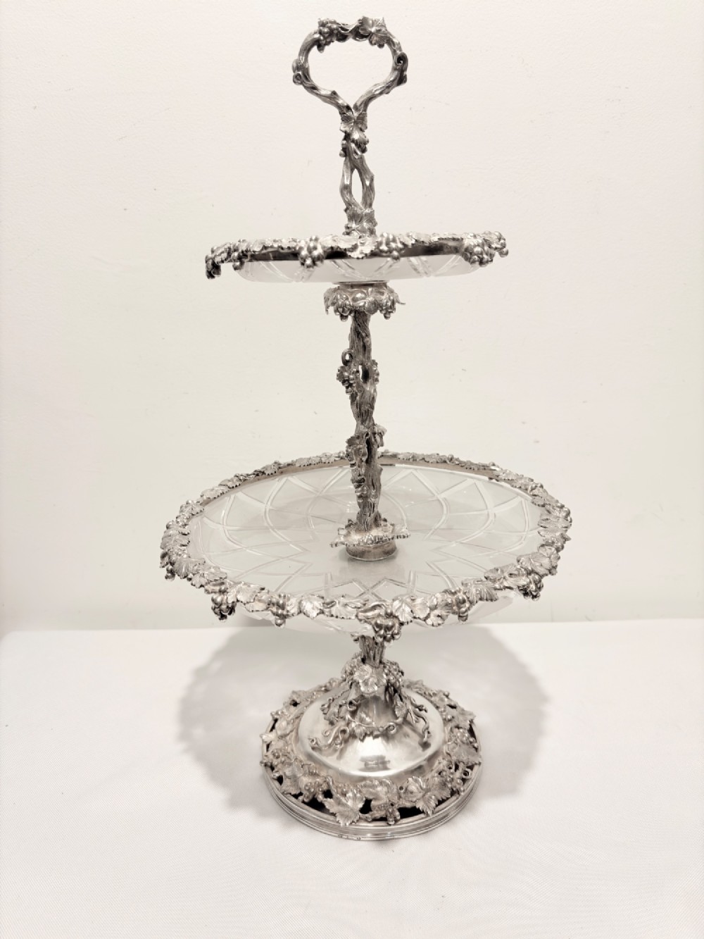 A Victorian silver-plated two-tiered epergne centerpiece featuring grapevine motifs and two cut glass trays.