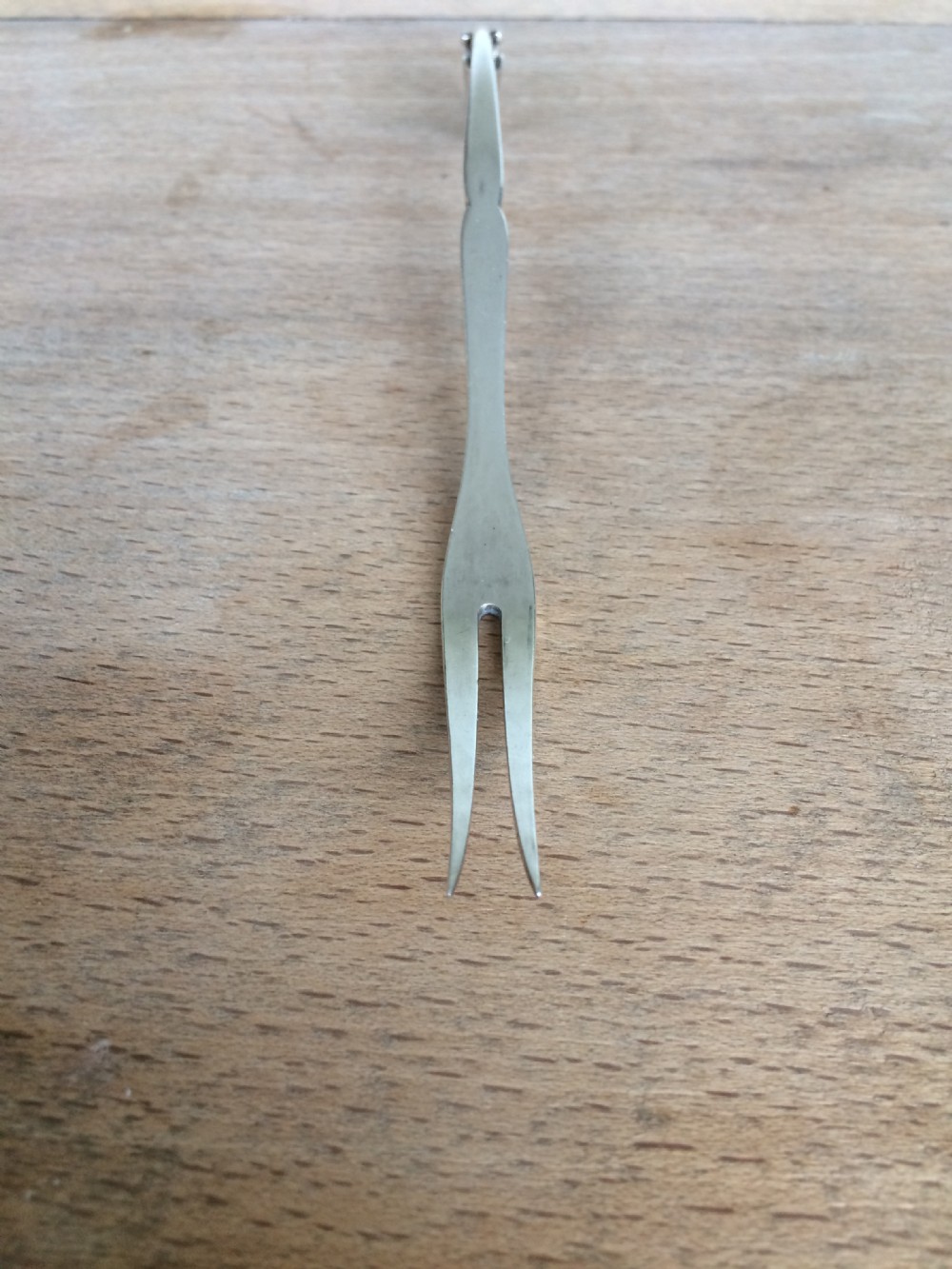 A Georg Jensen sterling silver Blossom pattern two-pronged cocktail fork resting in front of its original paper packaging box. View III