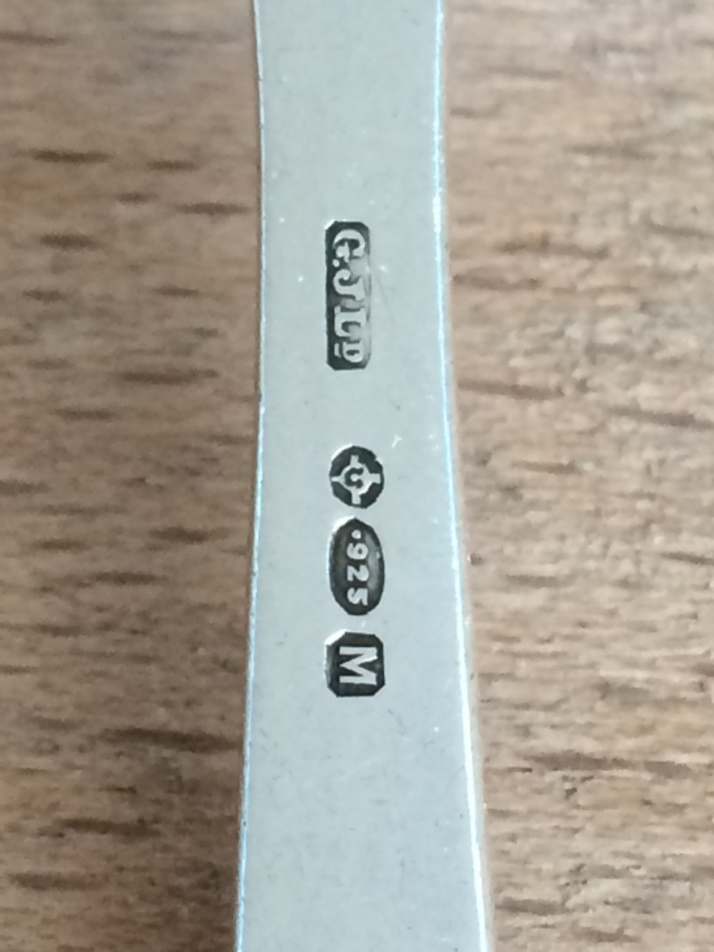A Georg Jensen sterling silver Blossom pattern two-pronged cocktail fork resting in front of its original paper packaging box. View V