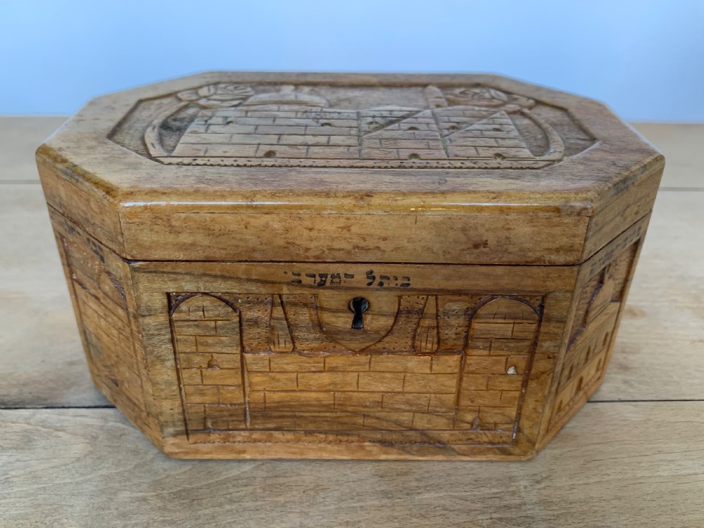 An octagonal carved olivewood Etrog box decorated with relief carvings of Jerusalem architecture and Hebrew lettering above a keyhole.