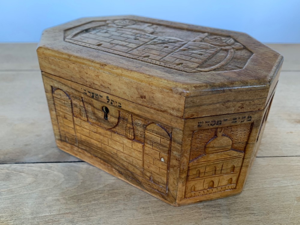 An octagonal carved olivewood Etrog box decorated with relief carvings of Jerusalem architecture and Hebrew lettering above a keyhole. View III