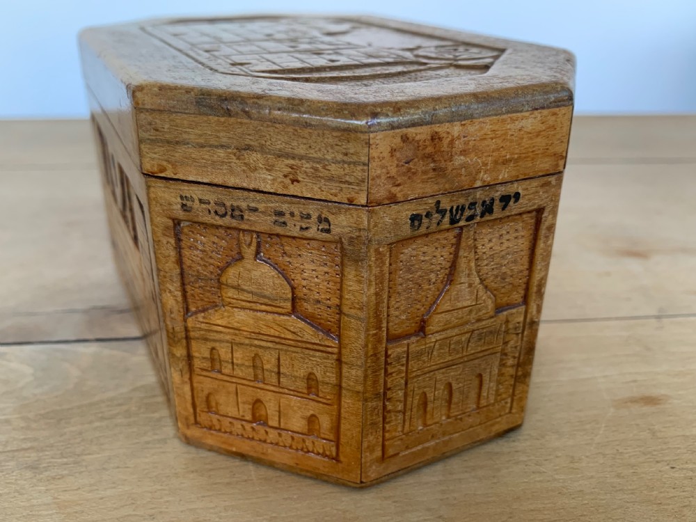 An octagonal carved olivewood Etrog box decorated with relief carvings of Jerusalem architecture and Hebrew lettering above a keyhole. View IV