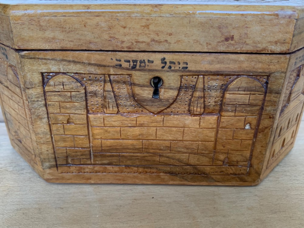 An octagonal carved olivewood Etrog box decorated with relief carvings of Jerusalem architecture and Hebrew lettering above a keyhole. View V