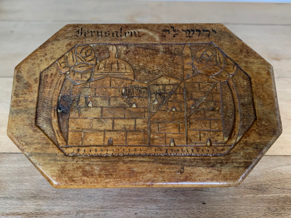 An octagonal carved olivewood Etrog box decorated with relief carvings of Jerusalem architecture and Hebrew lettering above a keyhole. View X