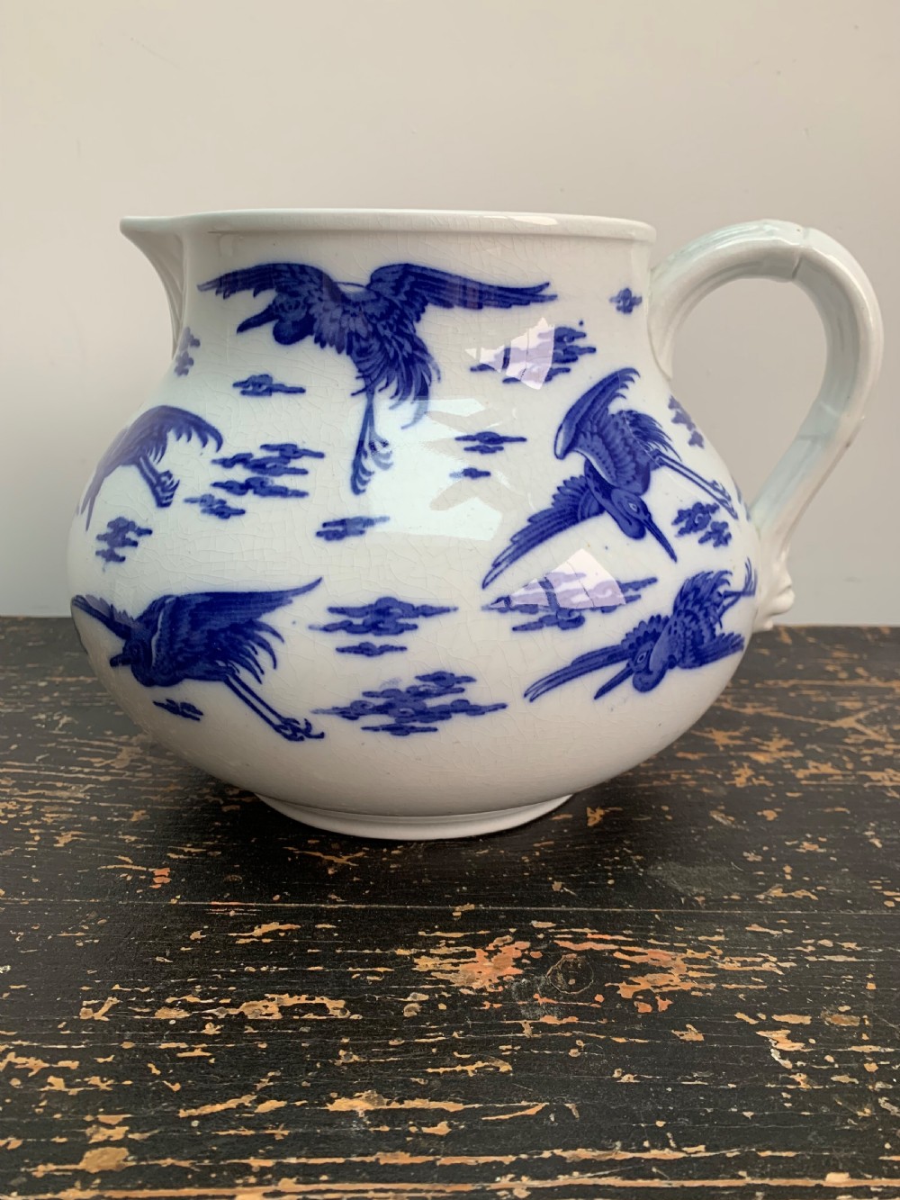 A bulbous white ceramic jug featuring transfer-printed blue flying cranes, a crackle glaze finish, and a moulded handle.