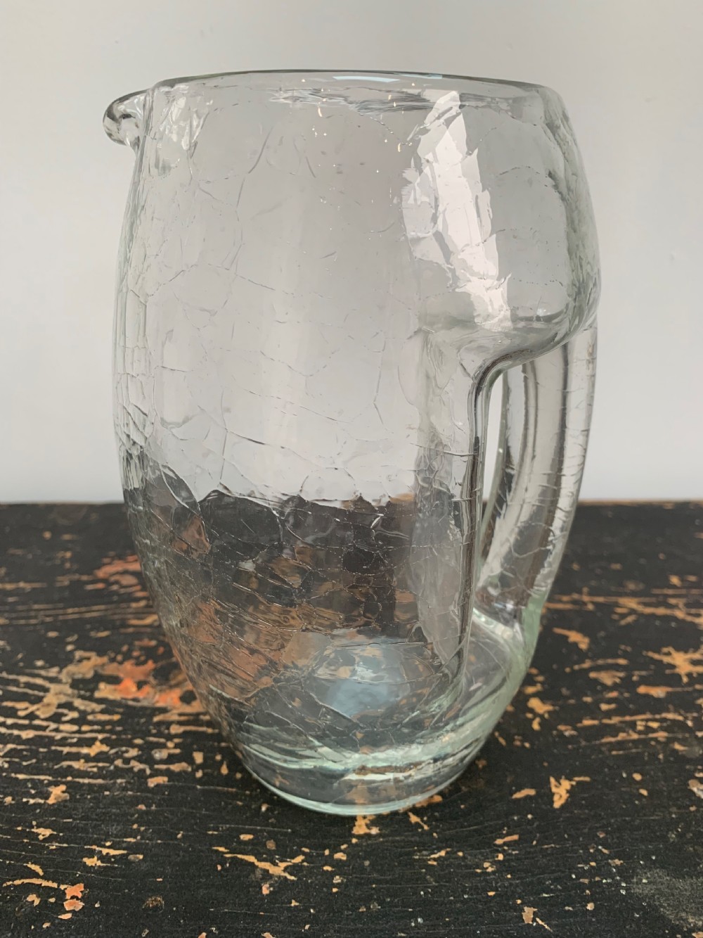 A clear blown glass jug featuring an all-over crackle finish and an integrated vertical handle.