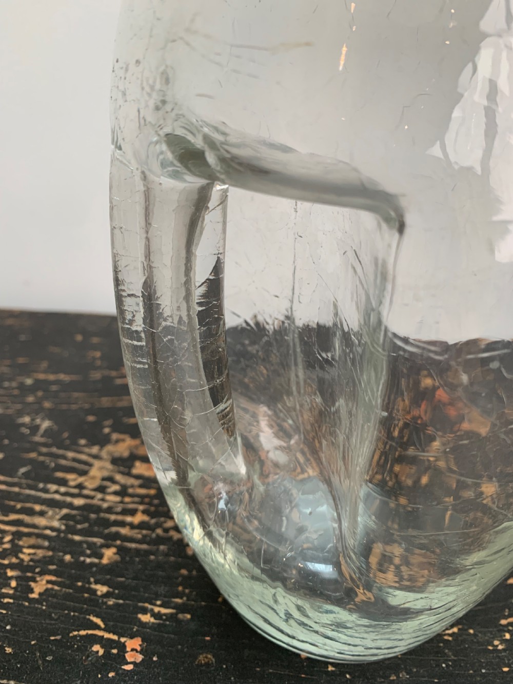 A clear blown glass jug featuring an all-over crackle finish and an integrated vertical handle. View VI