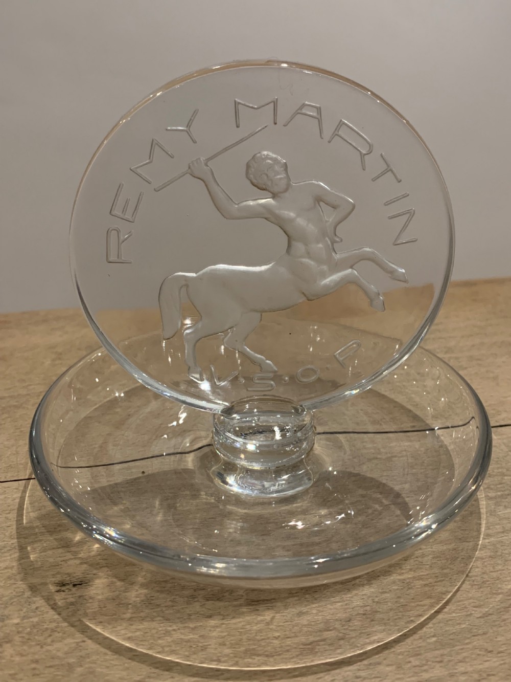 A clear glass Art Deco circular ashtray featuring an upright circular medallion with a frosted relief depicting a centaur holding a javelin above the lettering REMY MARTIN V.S.O.P.